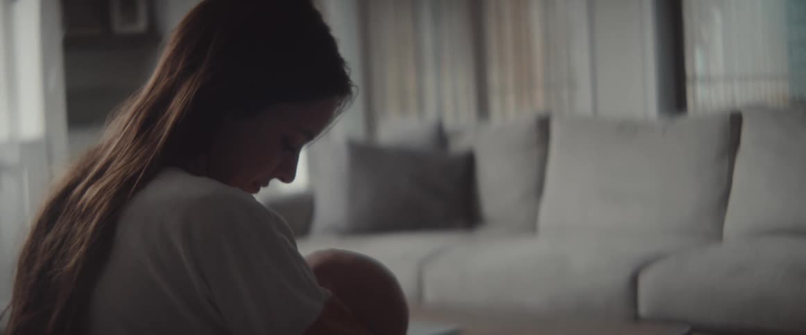 A woman in a room holding a baby with a table and a couch in the background