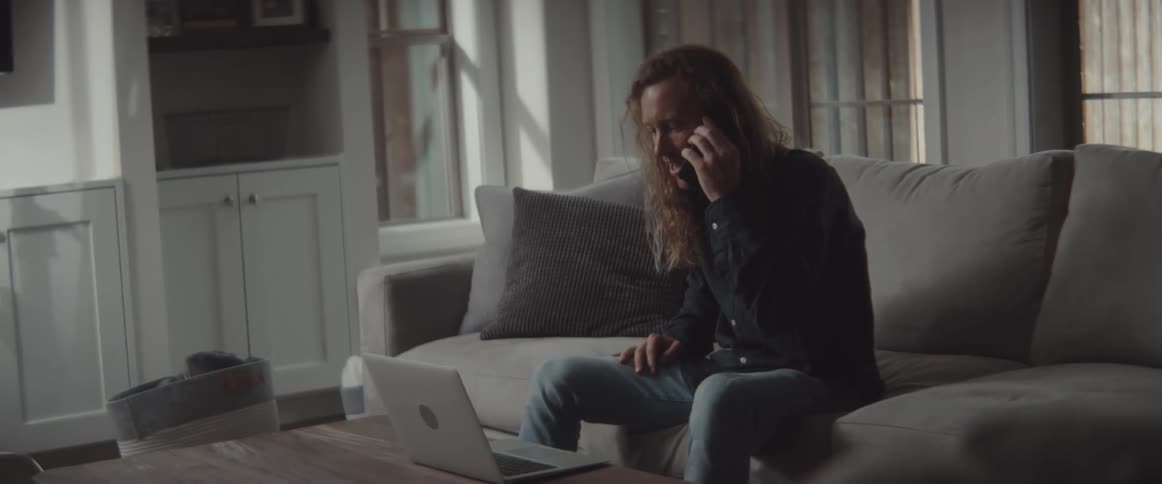 Man sitting on couch answers mobile phone and raises fist in celebration after talking a moment before returning to typing