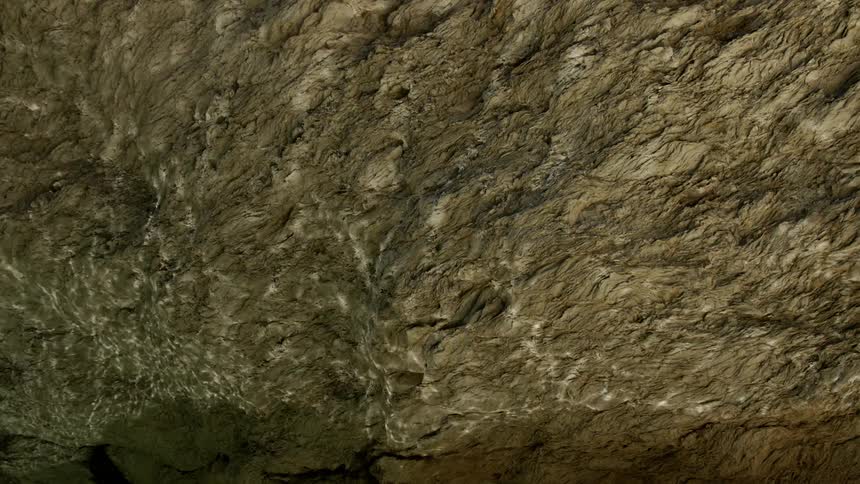 Rippling light reflects off a body of water onto the rock ceiling of a cavern