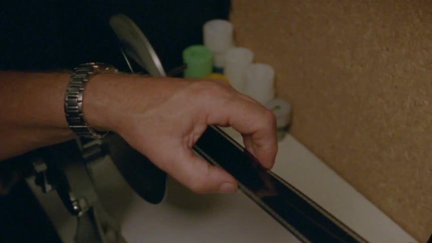 A person with a wristwatch in a room guiding a strip of film on a machine with a wheel