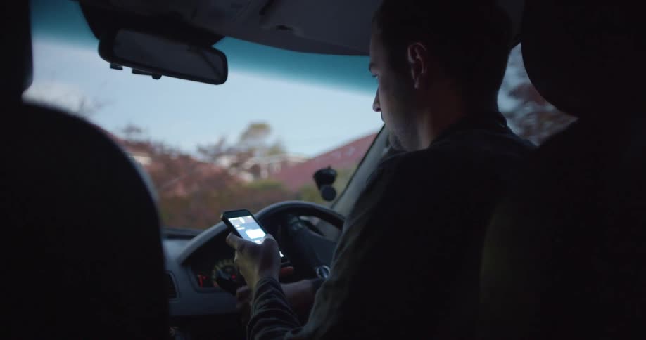 Man with a shirt drives car while using smartphone