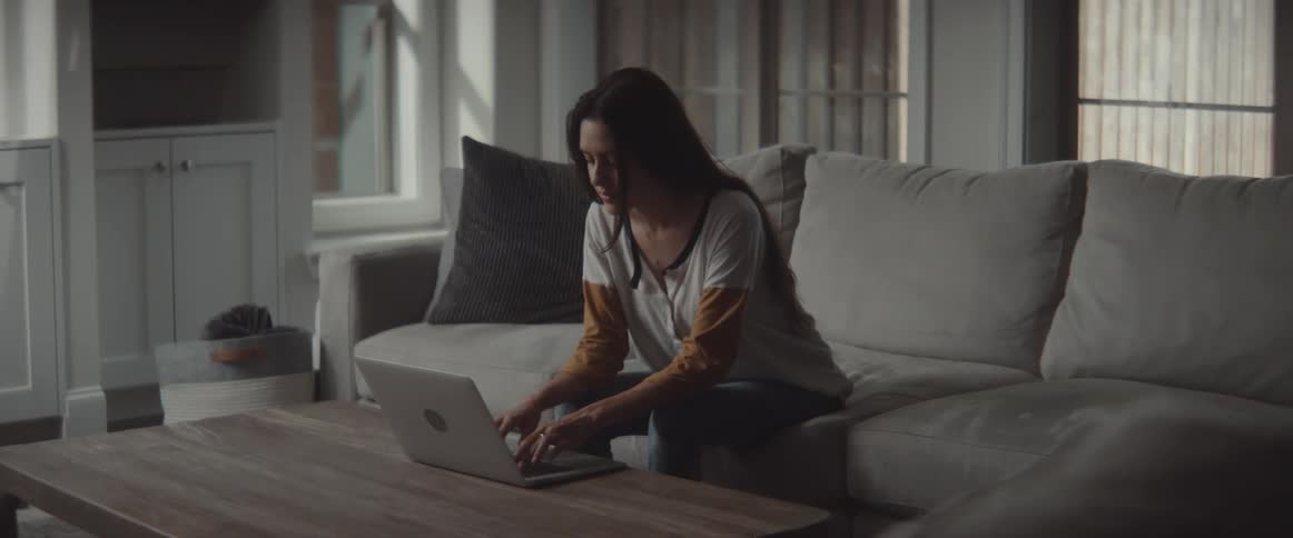 A woman in a room sitting on a couch typing on a laptop on a table