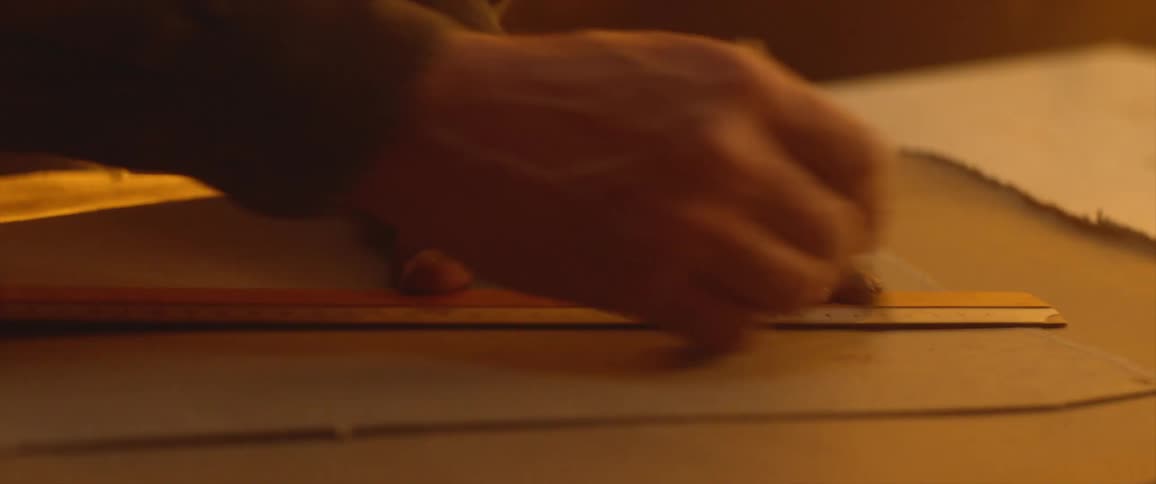 A man in an office draws on paper with a ruler