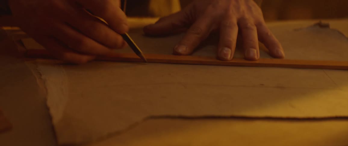 A man uses a ruler to draw straight lines on the back of a sheet of thick paper
