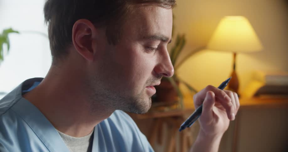 A nurse sitting indoors writes with a pen while speaking aloud
