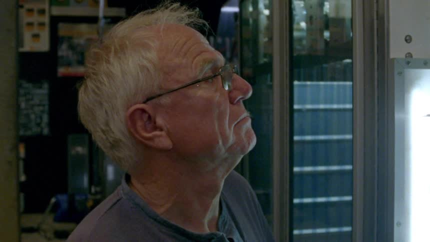 An elderly man stands and looks out a window