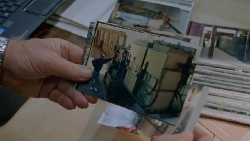 A man flips through a stack of photographs while sitting at his desk