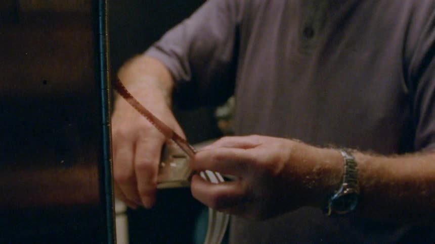 A man in a room with glasses and a wristwatch working on a strip of film