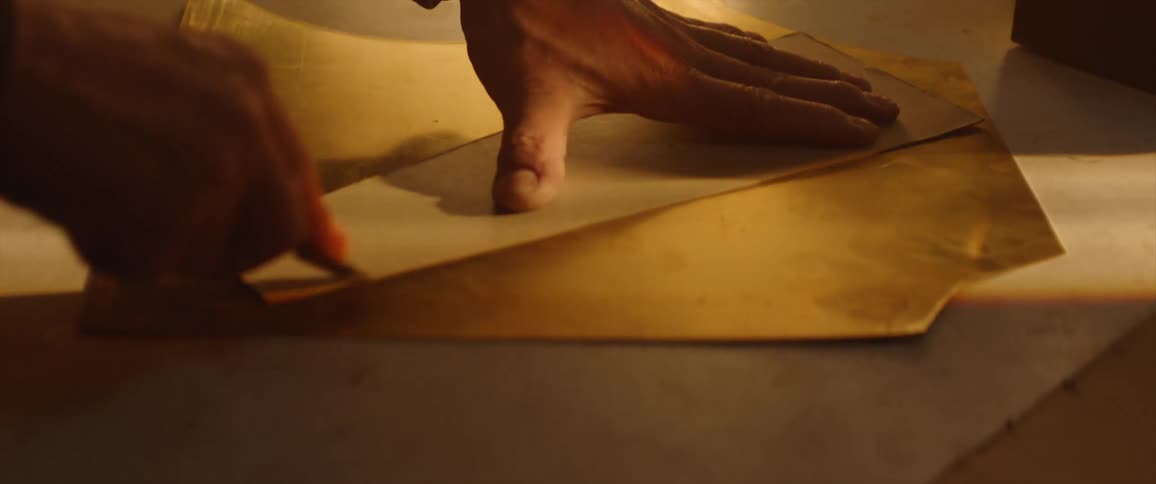 A person in a room cutting a piece of leather with a razor on a table