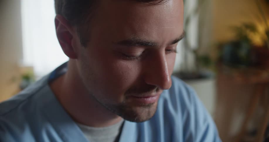 A man in a room with scrubs with a wall and window in the background