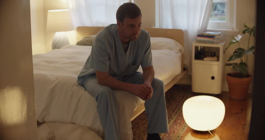 Man with a blue scrubs sits on bed next to golden dog in bedroom