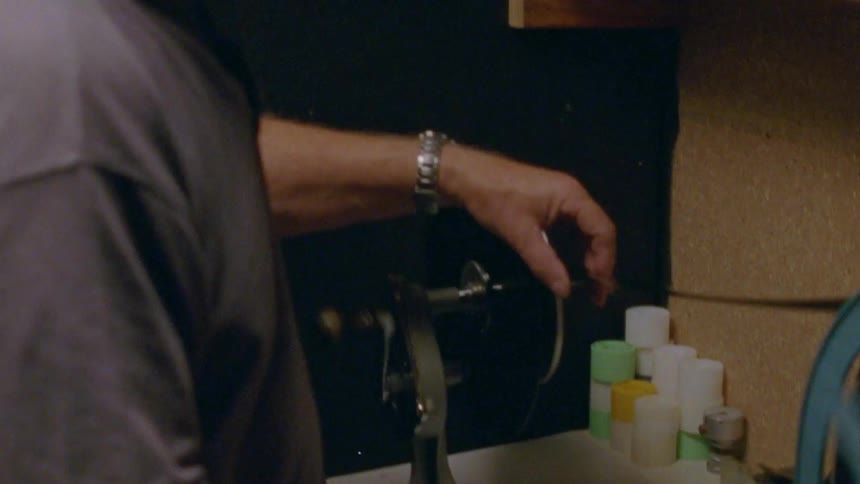 Elderly man reeling vintage film with a hand cranked machine over a workbench