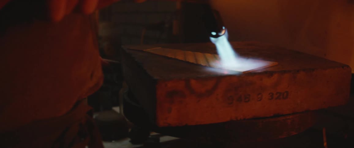 A person in a room using a blowtorch with fire on a piece of metal