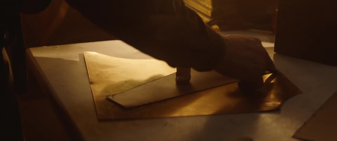 A person in a room cutting a piece of leather with a razor on a table
