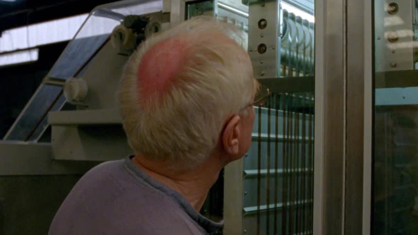 A man is watching a machine work behind the glass