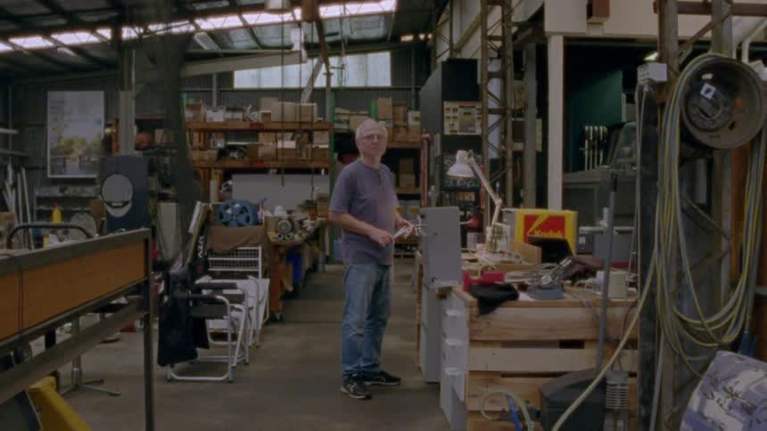 A man stands in a warehouse crowded with various tables and hoses