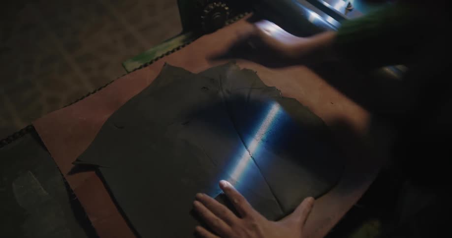 Sculptor flattening and scrapping a piece of clay inside a dimly lit workshop