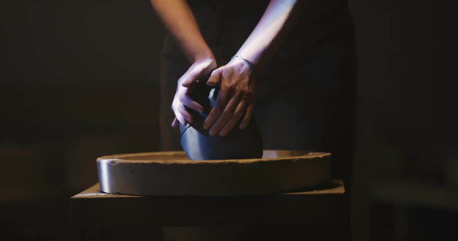 A woman kneads clay and then throws it down