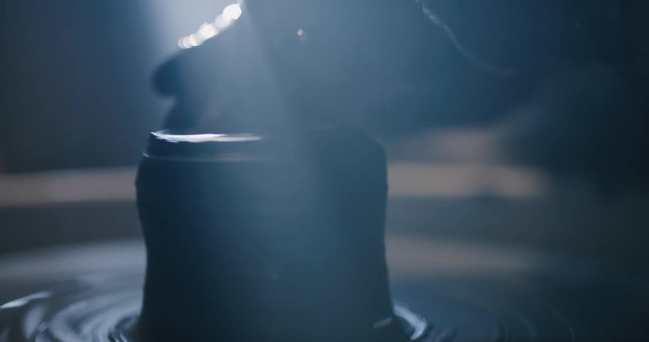 A sculpture shapes clay on a potters wheel in a dimly lit room during the day