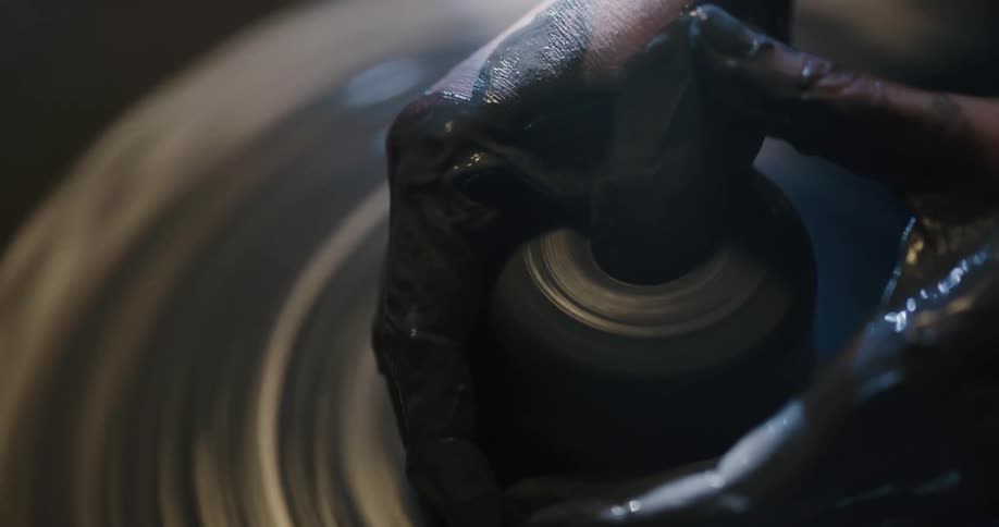 Person with hands coated in clay shapes clay on pottery wheel