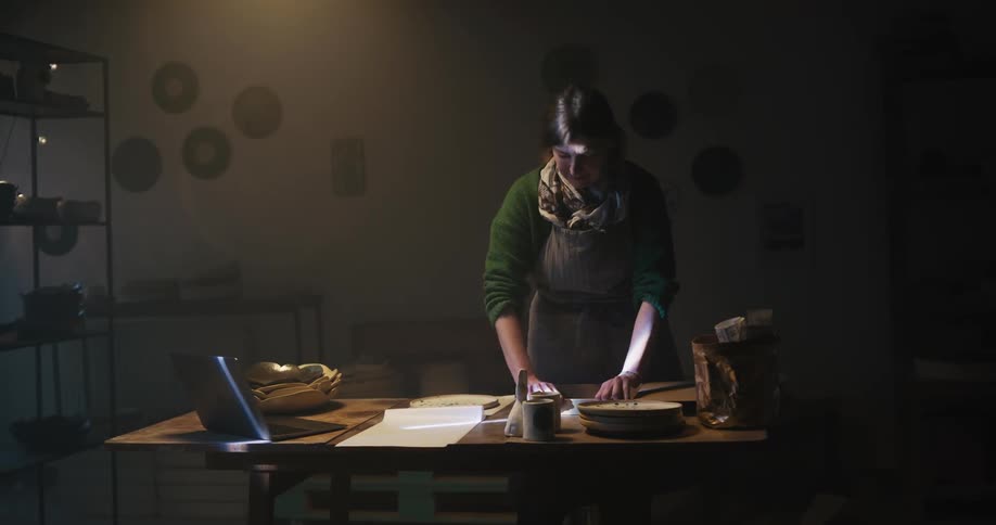 A woman folds up a cardboard box and packages a ceramic plate for shipping