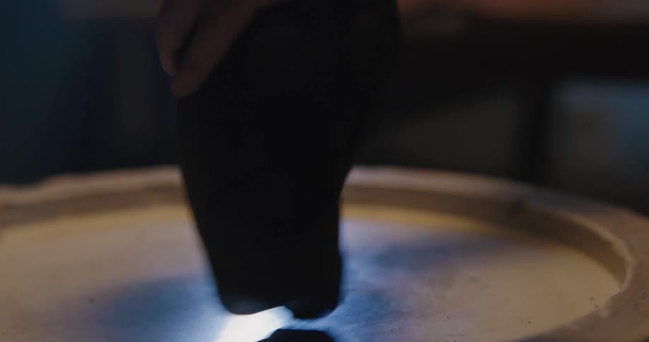 Sunlight from a window shines on a woman kneading a large chunk of clay