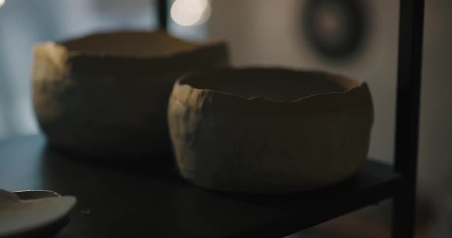 A person in a room taking pottery from a shelf with a wall in the background