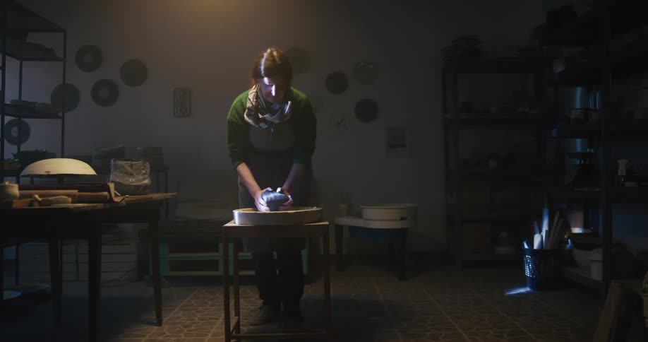 A woman slams a piece of clay on the table repeatedly