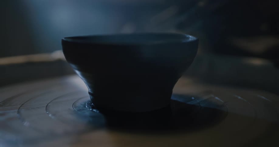 A person in a room shaping clay on a spinning wheel
