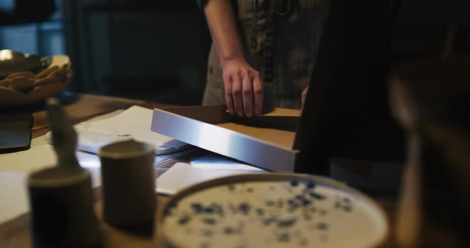 A person in a room assembling a box and putting something wrapped in paper in it