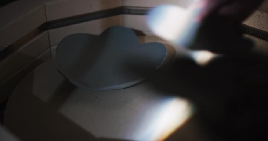Person places bowls in kiln to be fired in dim room lit by beam of sunlight