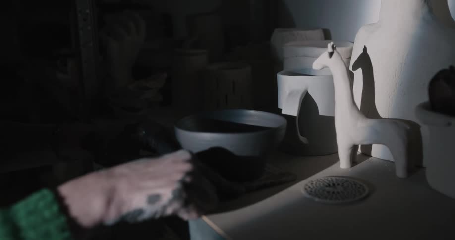 A person in a room putting pottery on a shelf with a wall in the background