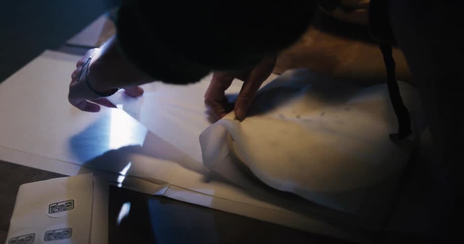A person wraps a ceramic dish in paper before securing the paper with a sticker and placing the wrapped dish in a box