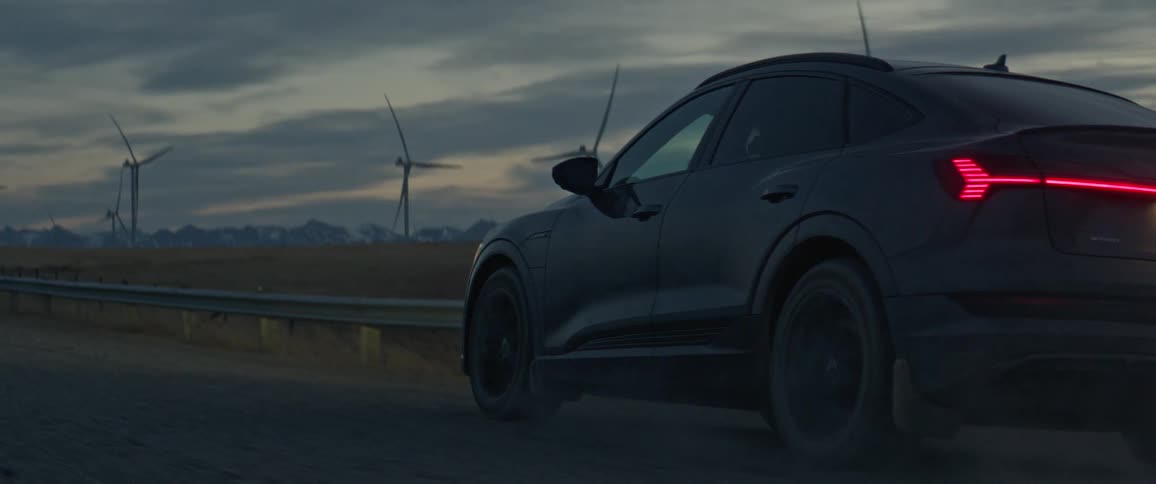 Black car driving on a dirt road neara wind farm in the morning