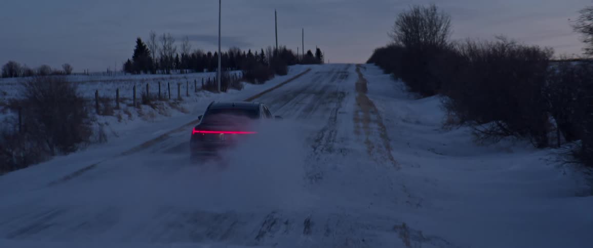 Dark grey audi car drives on snowy country road in the countryside at dusk