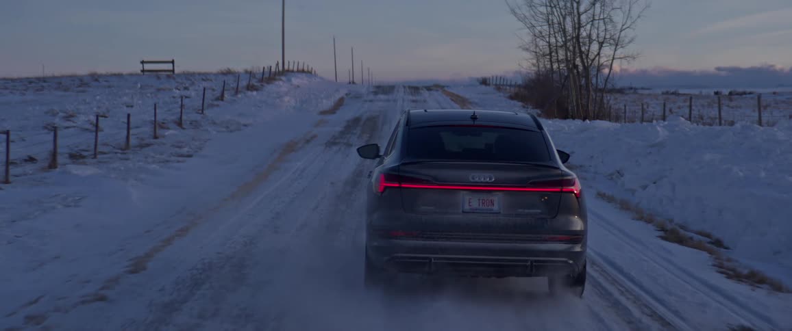 A car is driving down a rural road in winter at dusk