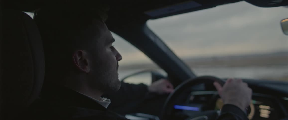 A man in a vehicle driving and turning the steering wheel with the sky and clouds in the background