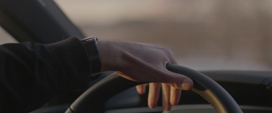 Man hands on the steering wheel of a car driving at sunset