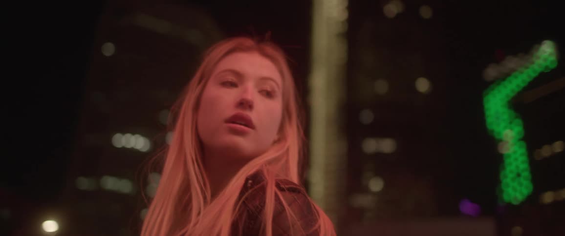 Blonde woman with a black leather jacket looks backs over her shoulder in the city at night