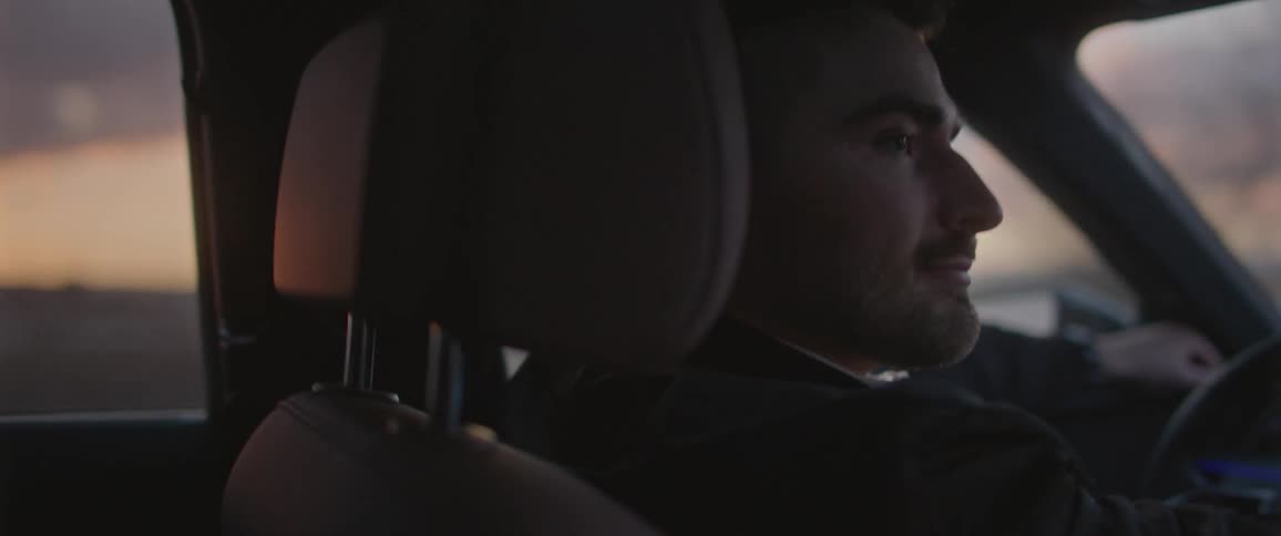 Man driving a car on the countryside at sunset talks to the person sitting on the passenger seat