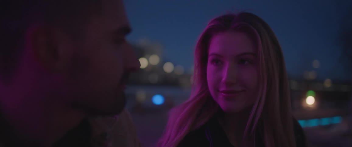 A young woman is smiling and looking at a man as he talks