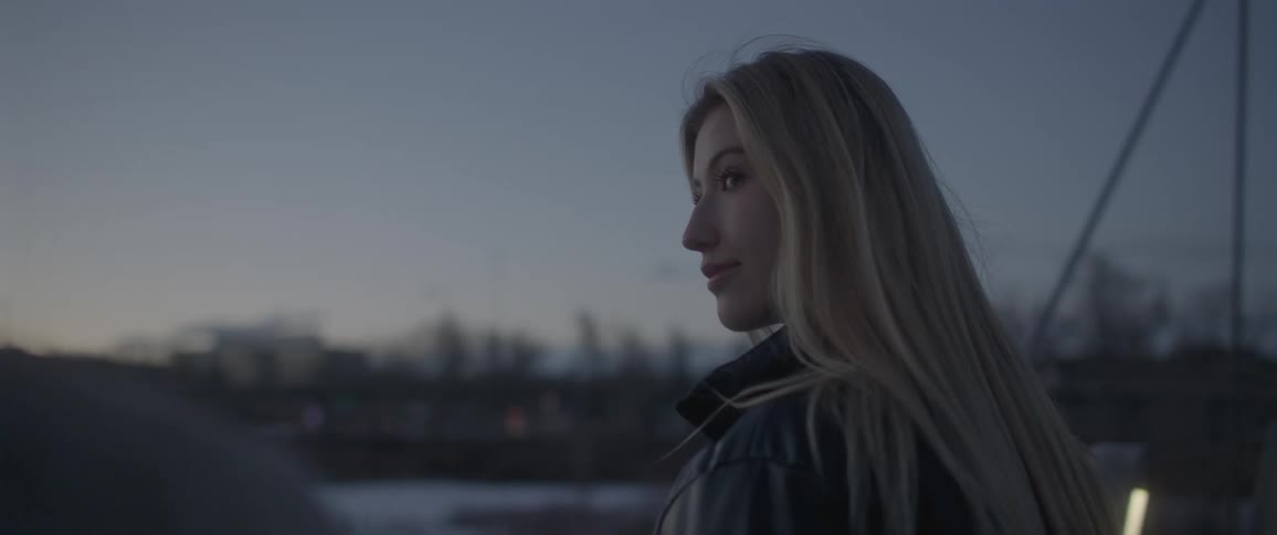 Blonde girl with black leather jacket looks at man on the bridge at dusk