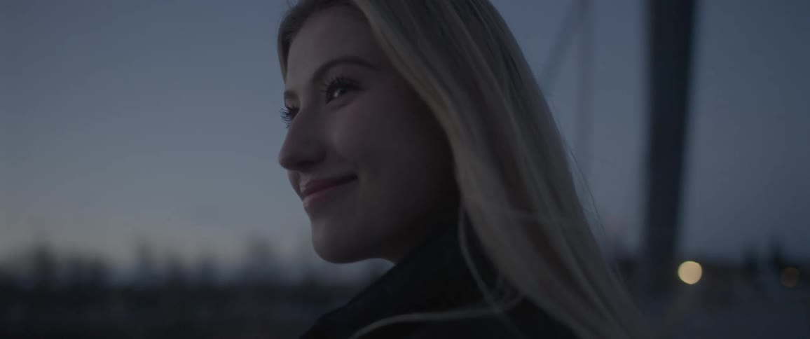 Blonde woman with a black leather jacket looks at her boyfriend smiling on the bridge at dusk