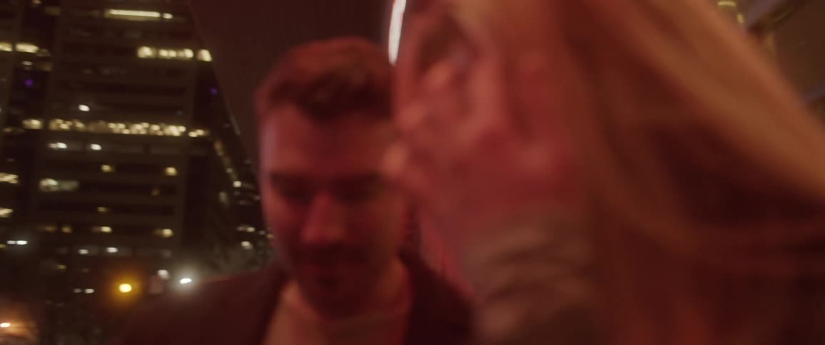 A man and woman stand outside in a metropolitan area and look around at their surroundings