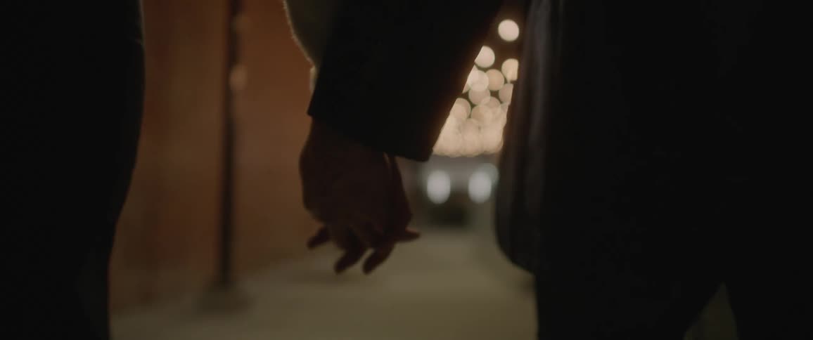 Young couple walk holding hands under the lights on a city street at night
