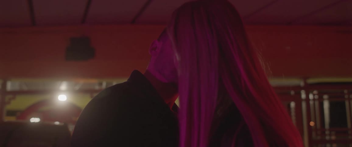 Couple stands bathed by purple lights kissing and smiling