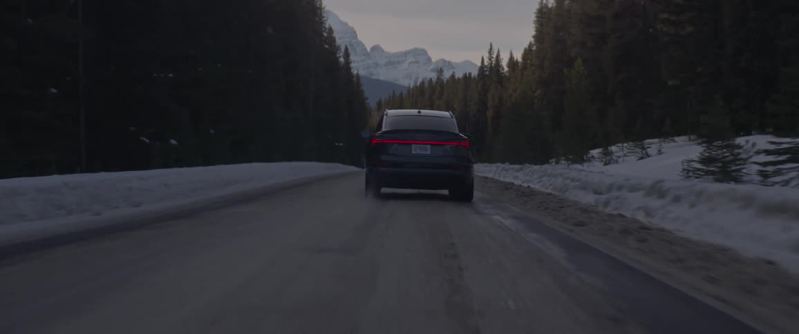A vehicle travels a snow dusted rural road surrounded by trees