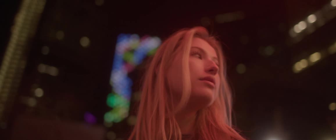 A woman standing in a city with buildings lights and the sky in the background