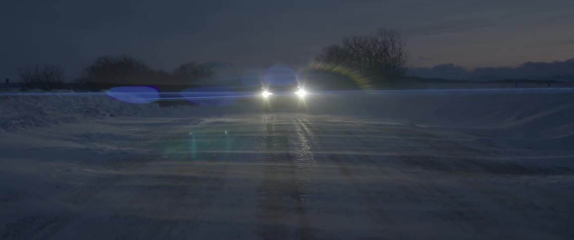 A car is driving on a road at night in winter