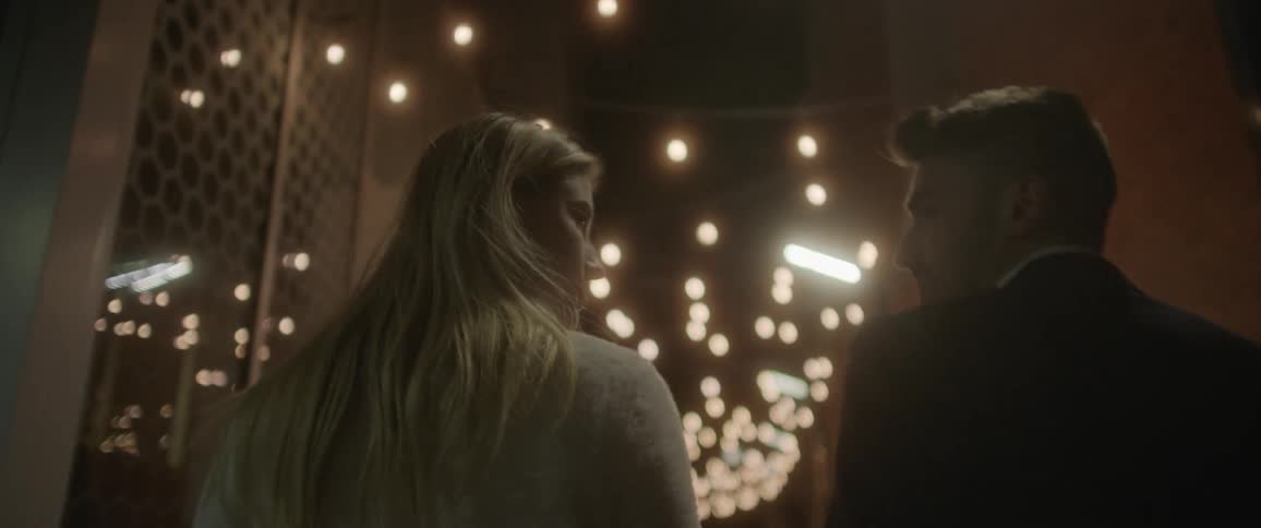 A man and woman talk as they walk down a lit up city street